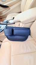 DriveTidy car seat gap filler organizer in black faux leather, fitted into the gap beside a beige car seat with two front pockets facing up.