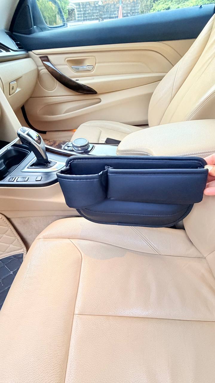 Angled view of the DriveTidy organizer being fitted into the seat gap beside the center console, showing its two pockets from the side.