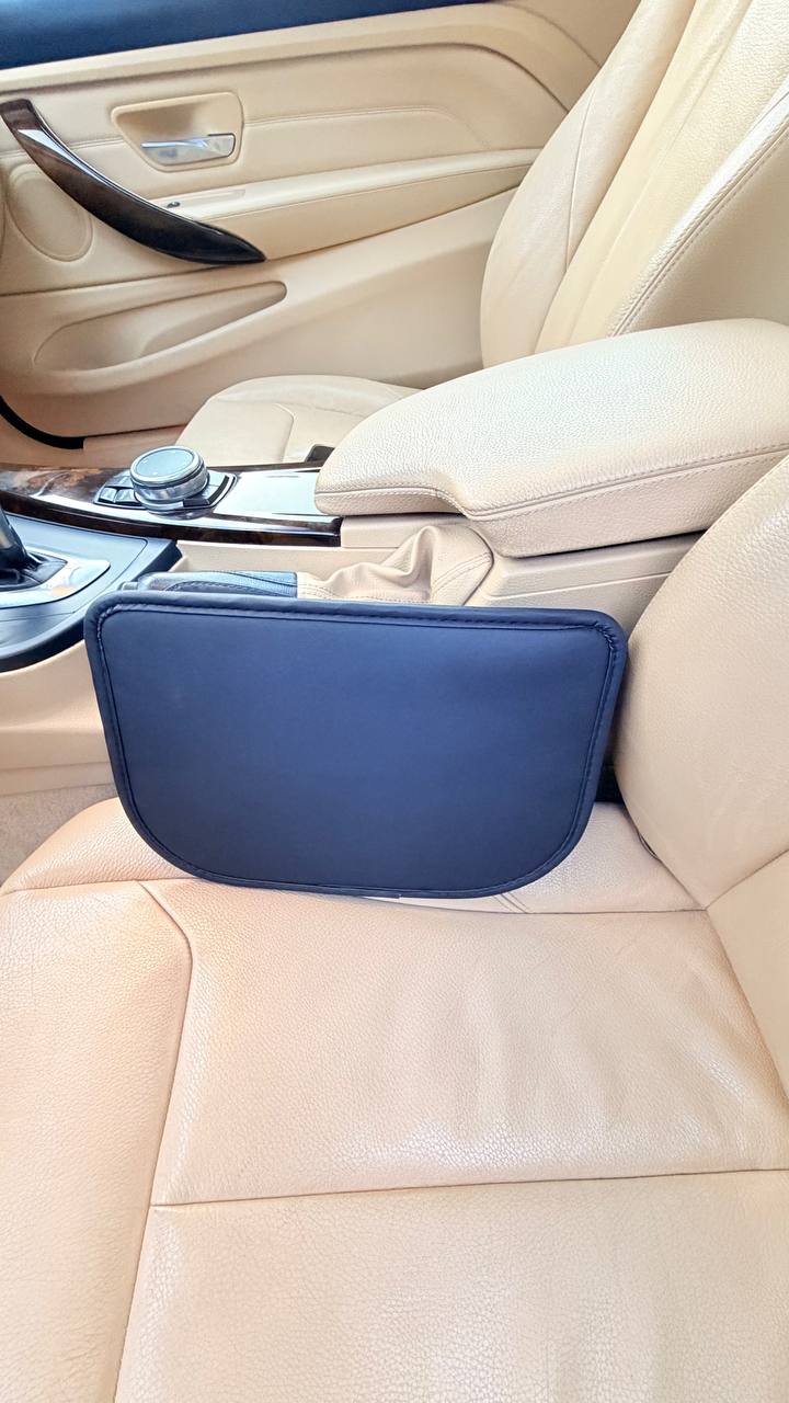 Close-up of the DriveTidy organizer's smooth black faux-leather back panel sitting flush in the seat gap against the beige leather seat.